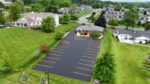 This overhead view captures a freshly sealed commercial parking lot surrounding a multi-story building, treated with a premium, sand-fortified rubberized asphalt emulsion. Engineered for long-lasting performance, this polymer-enhanced sealer reconditions and texturizes aged pavement while forming a waterproof barrier resistant to oil and gas damage. The result is a rich satin black surface with bright, well-defined striping. Ideal for high-traffic environments, it offers a two-coat coverage rate of 30 to 40 sq. ft. per gallon and enhances both durability and aesthetics.