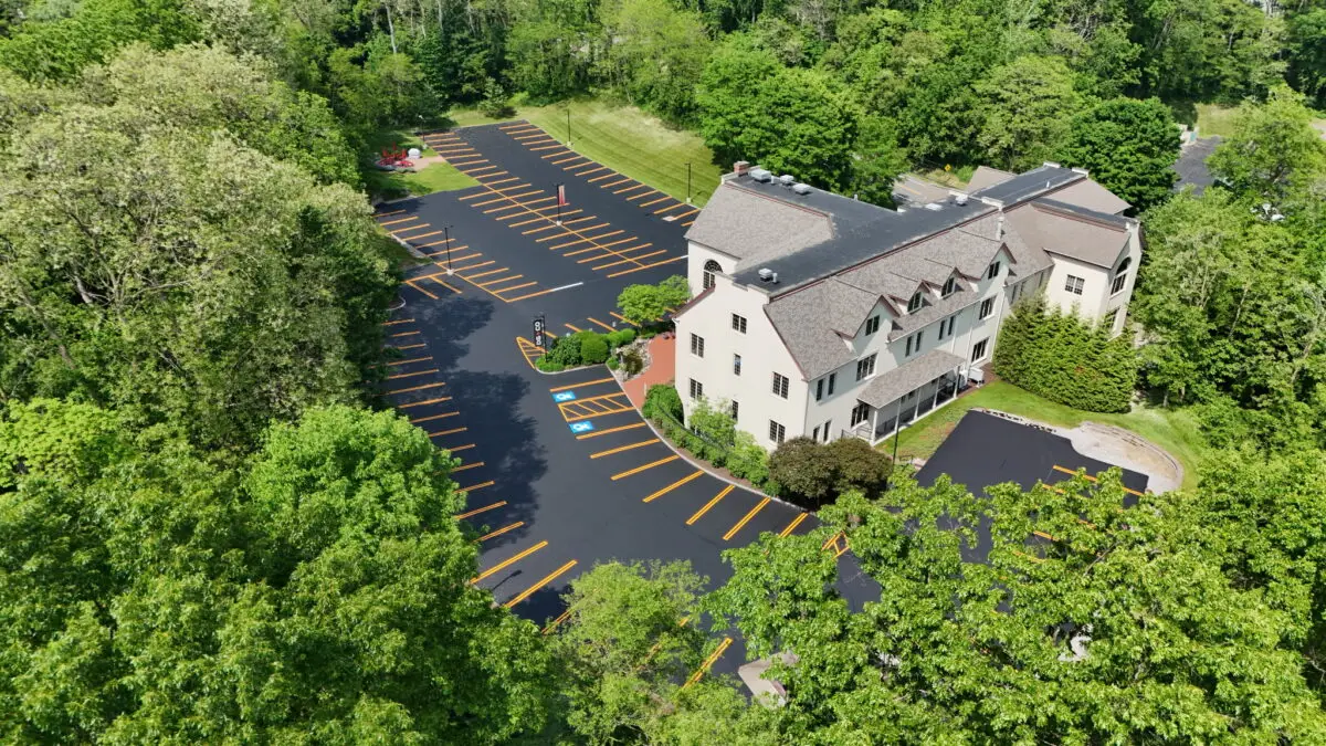 Large commercial parking lot with fresh blacktop sealer and crisp yellow striping around a multi-story office building.